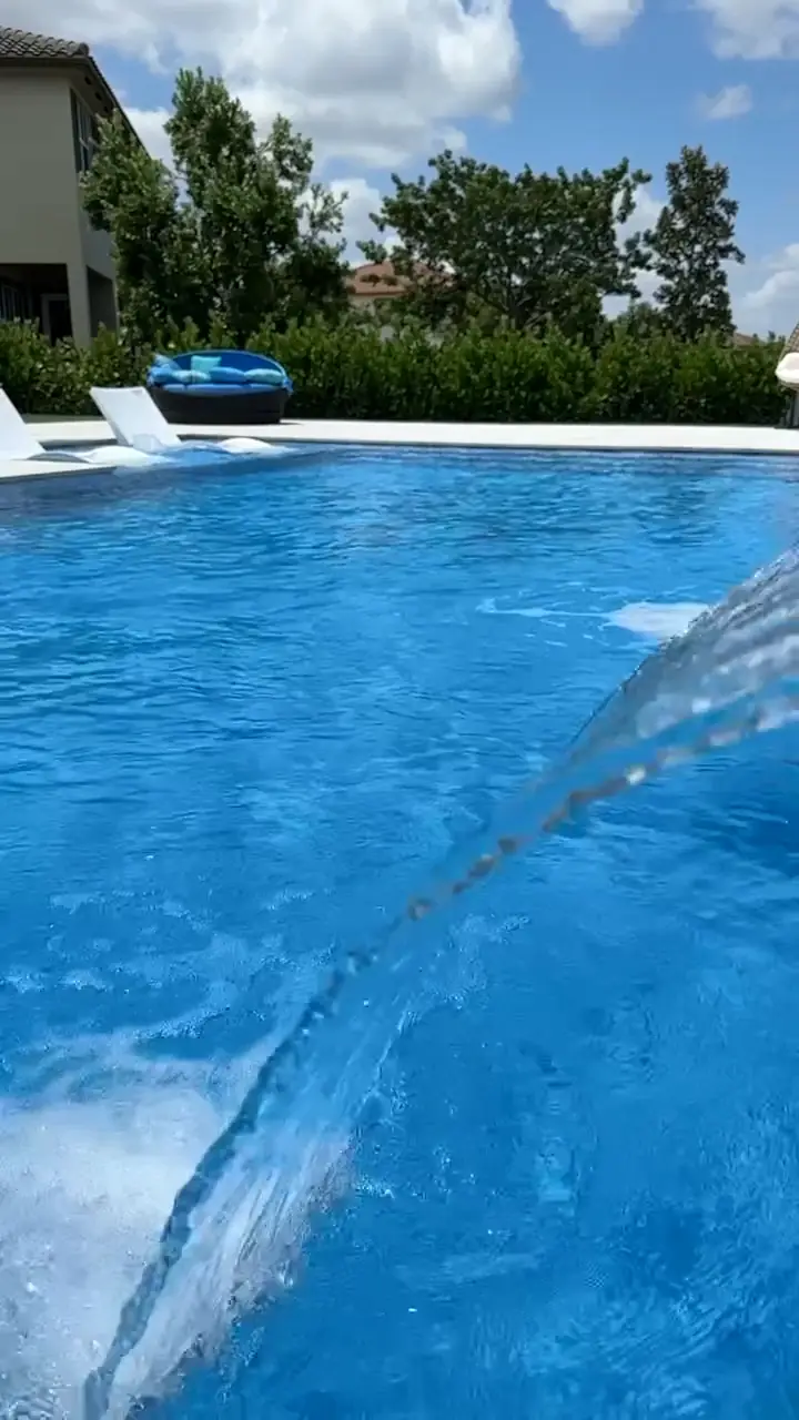 A deck jet arcing into a bright turquoise pool, with loungers, a hedge and palms behind