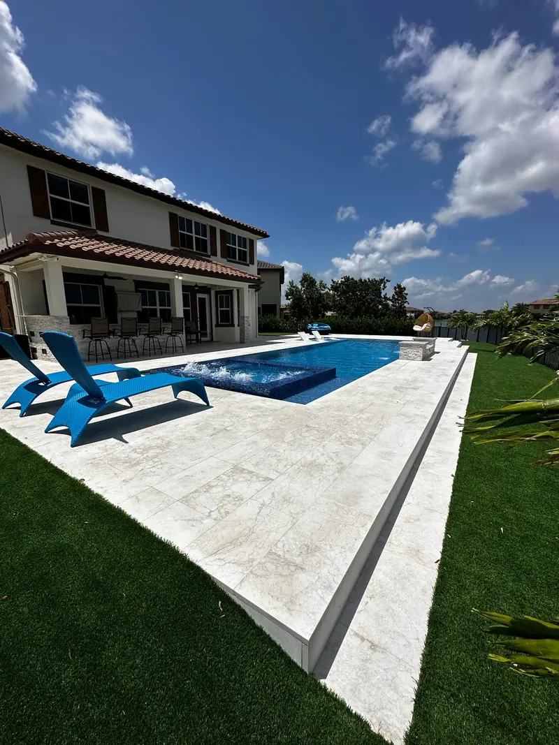 Pool with blue loungers on a white deck beside a two-story home