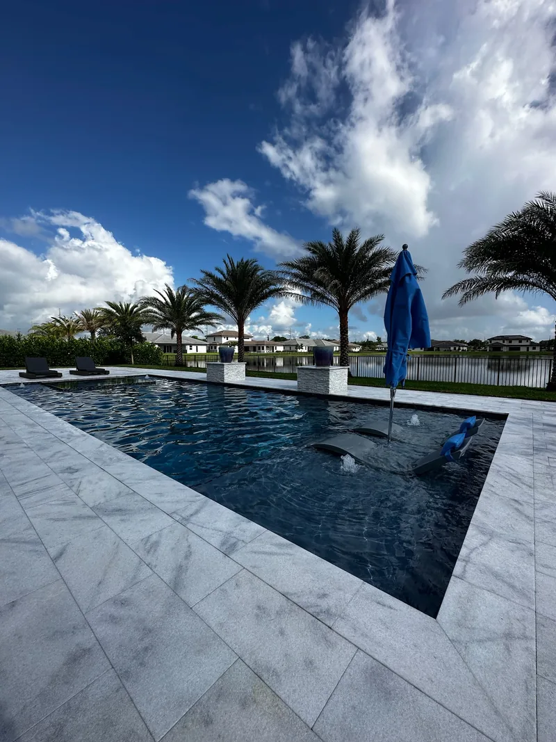 Dark-finish pool with palms, an umbrella and in-pool loungers