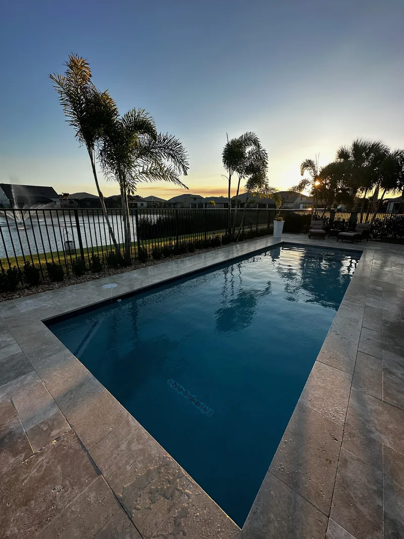 Pool at dusk with a travertine deck and palm silhouettes