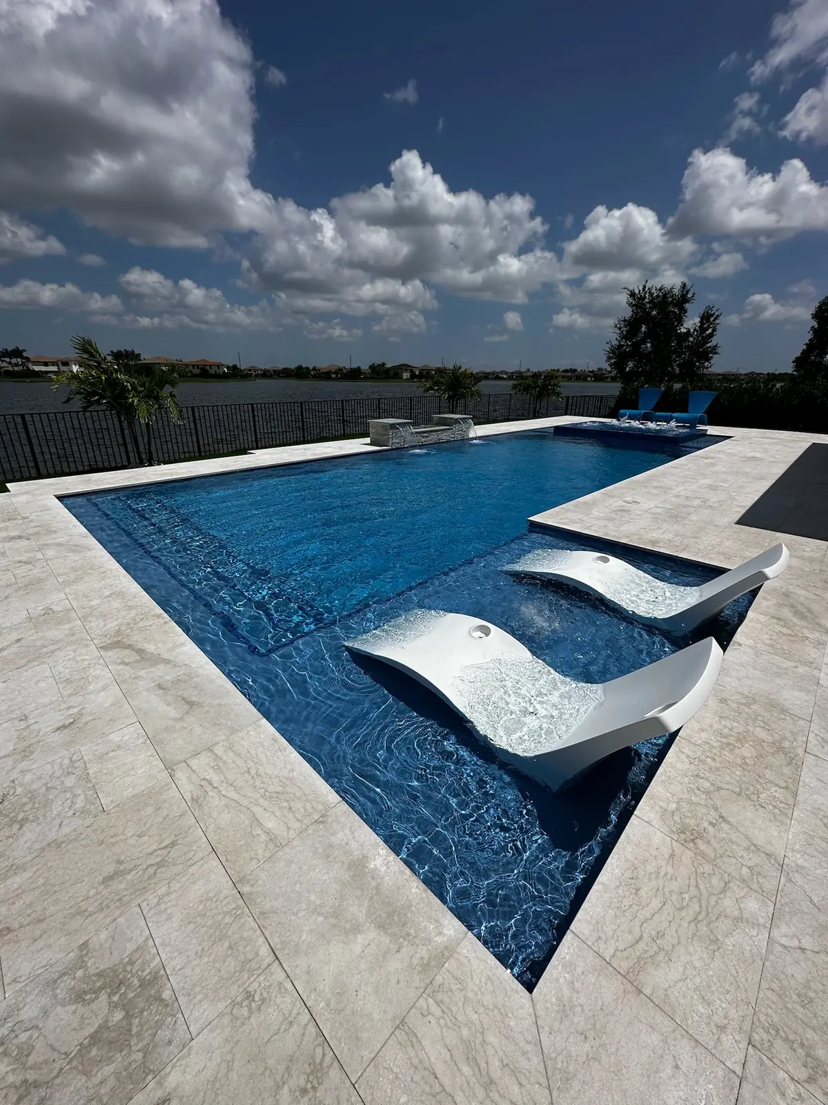 Two white in-pool loungers on a sun shelf, with a lake beyond the deck