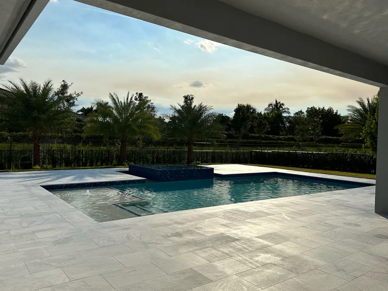 View from a covered lanai of a pool and raised spa at dusk