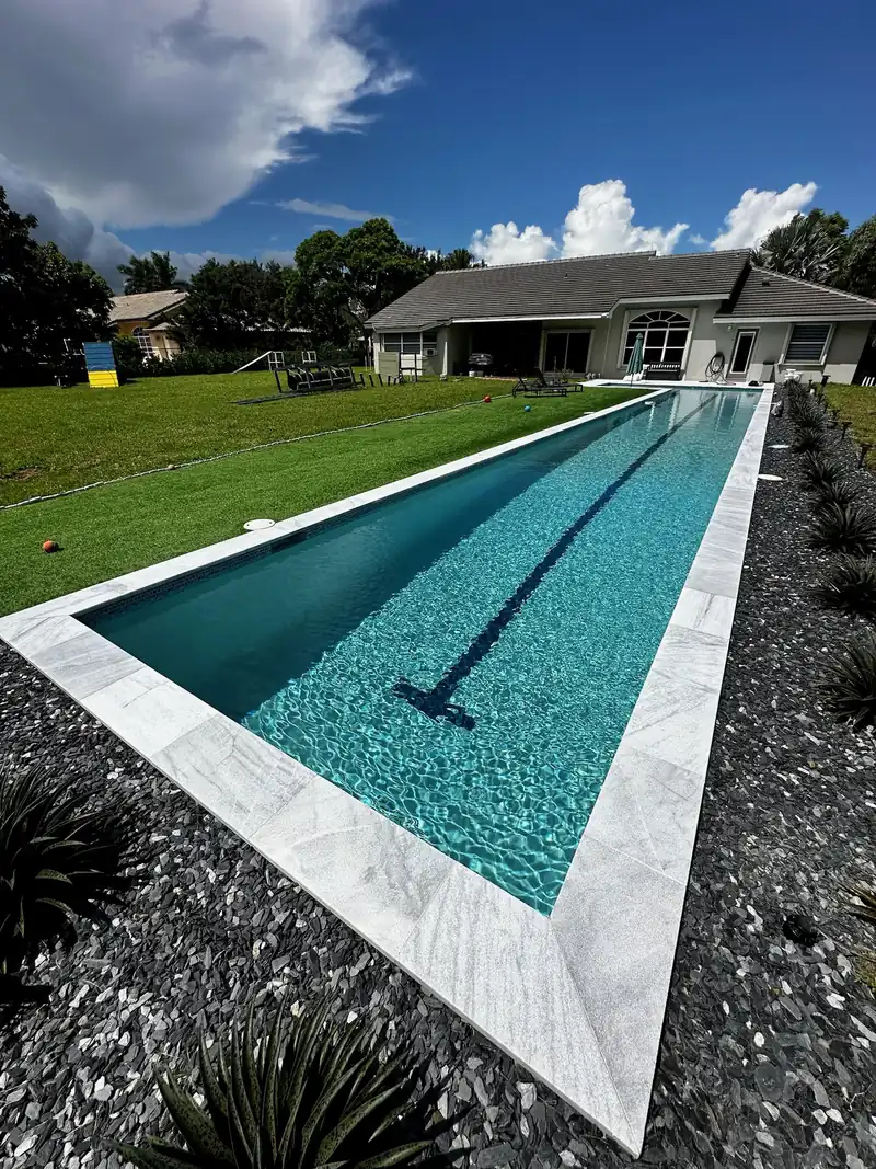 Long lap pool with gravel landscaping and a house beyond