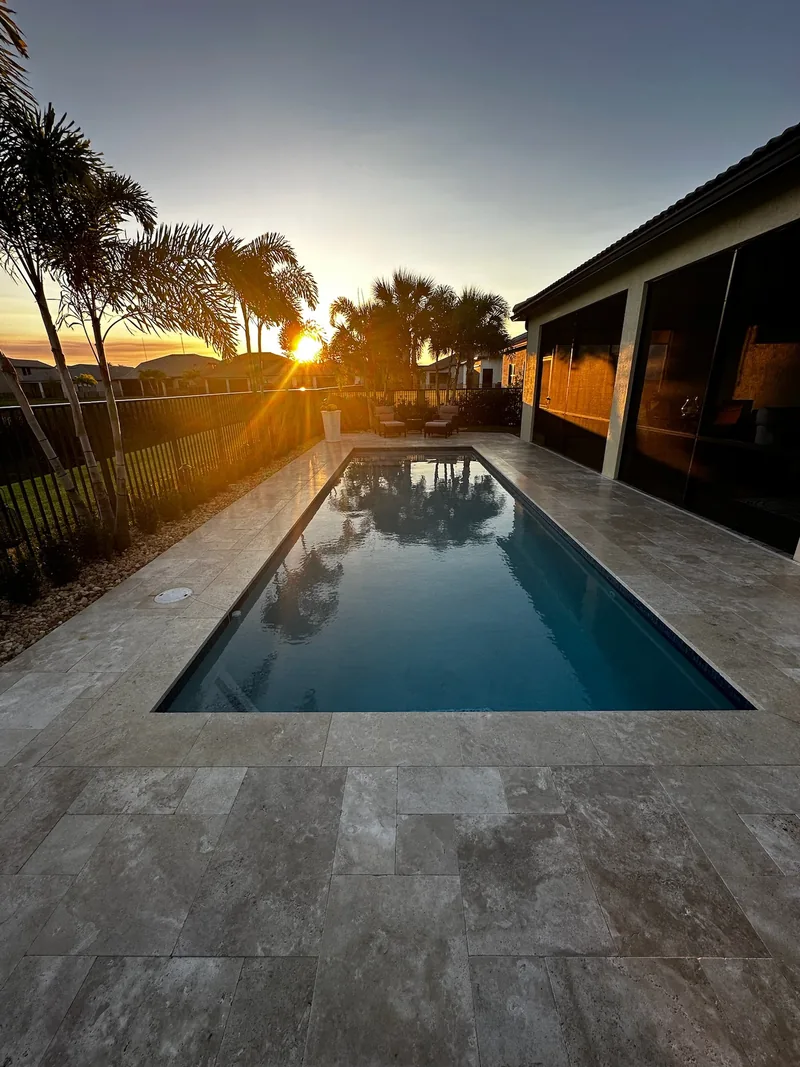 Long pool at golden hour with sun glare over a stone deck