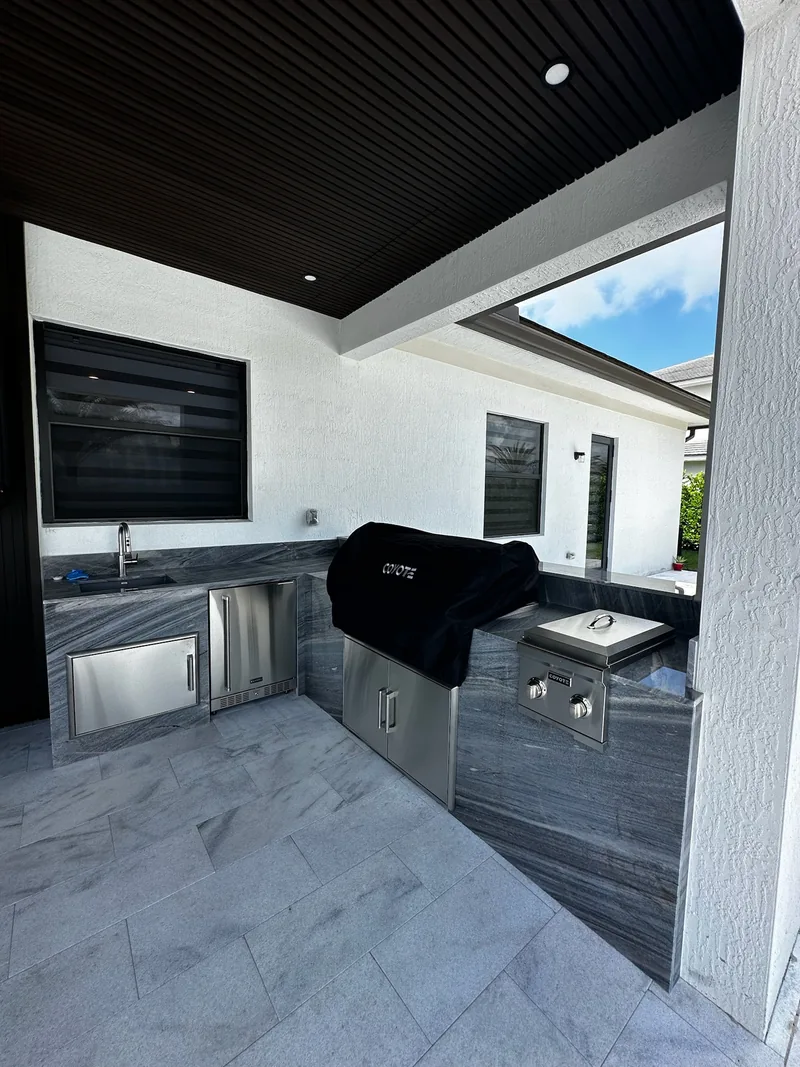 Outdoor kitchen with a built-in grill under a dark wood ceiling
