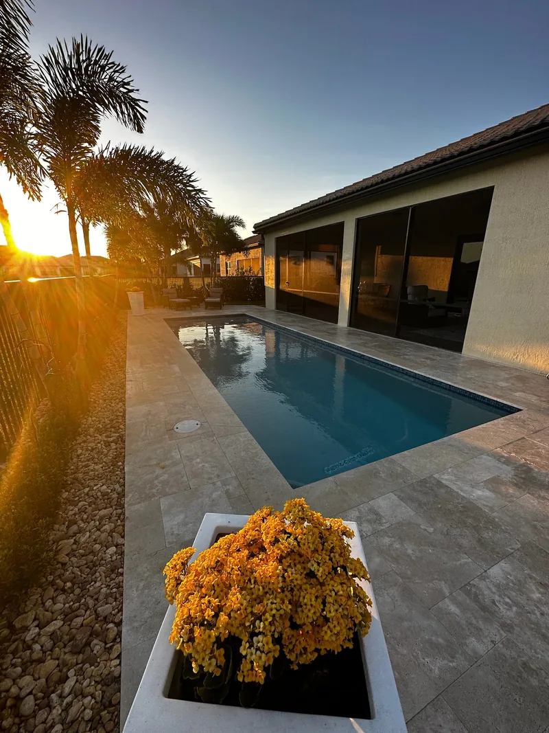 Pool beside a covered lanai at golden hour, with a yellow flower planter