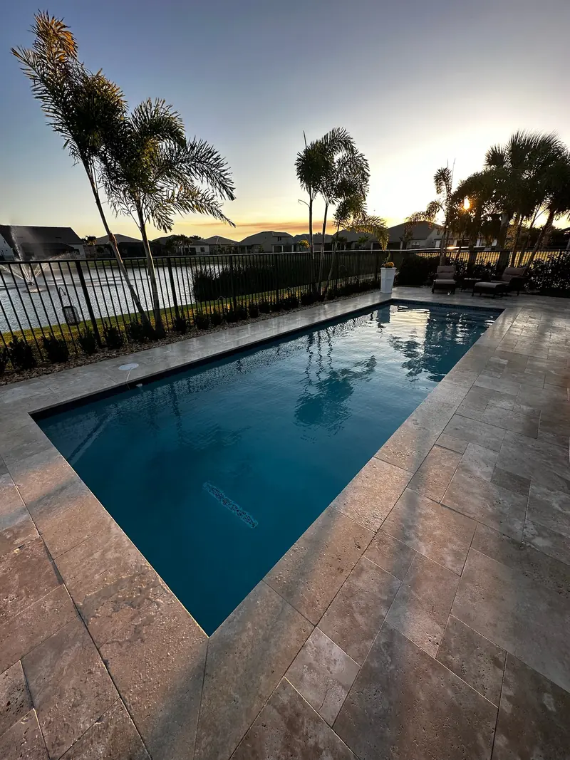 Pool at sunset with a warm stone deck and palm silhouettes
