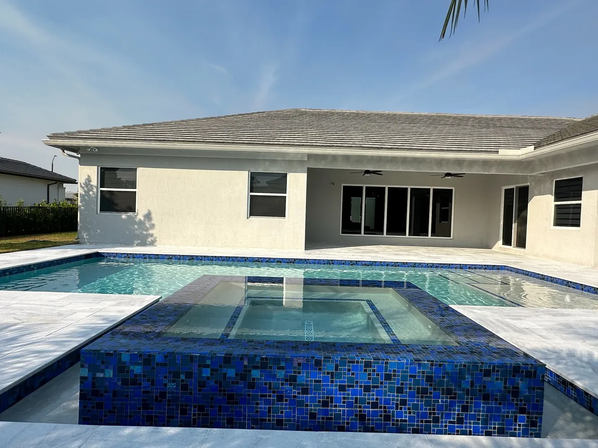 Raised spa faced in blue glass mosaic in front of a white single-story home