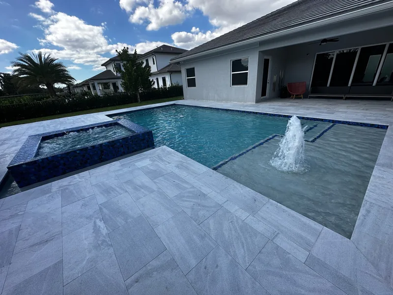 Raised spa and a bubbler on a sun shelf, with a white travertine deck and a white home