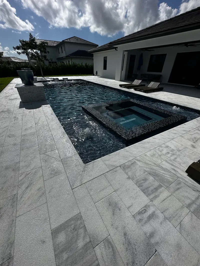 Raised spa inside a dark-finish pool with a white travertine deck