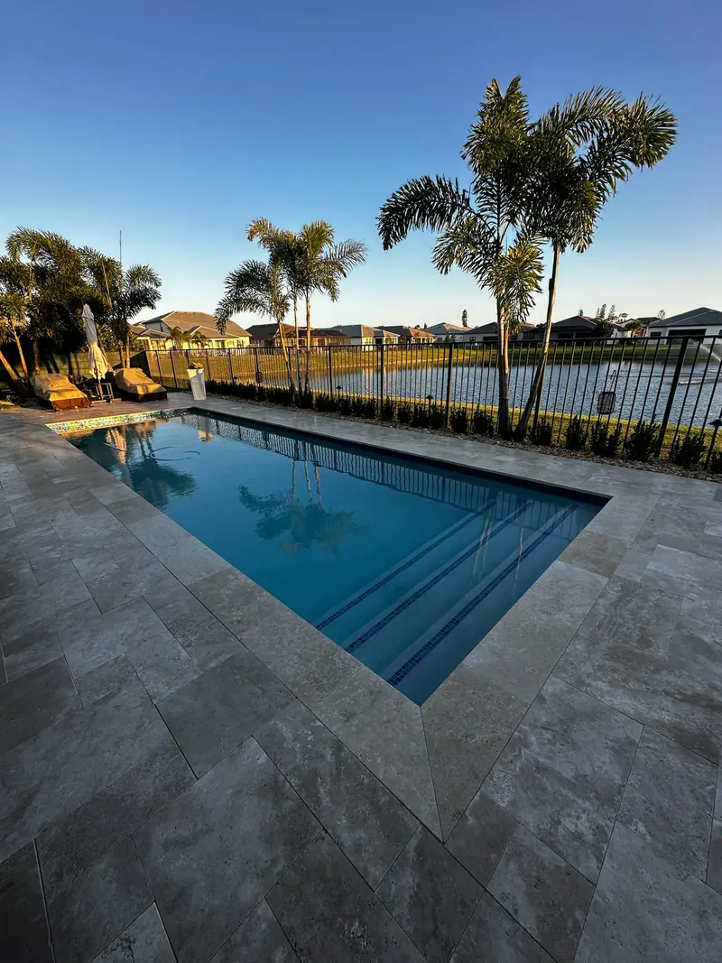 Pool at sunset with a warm travertine deck, palms and a lake fence