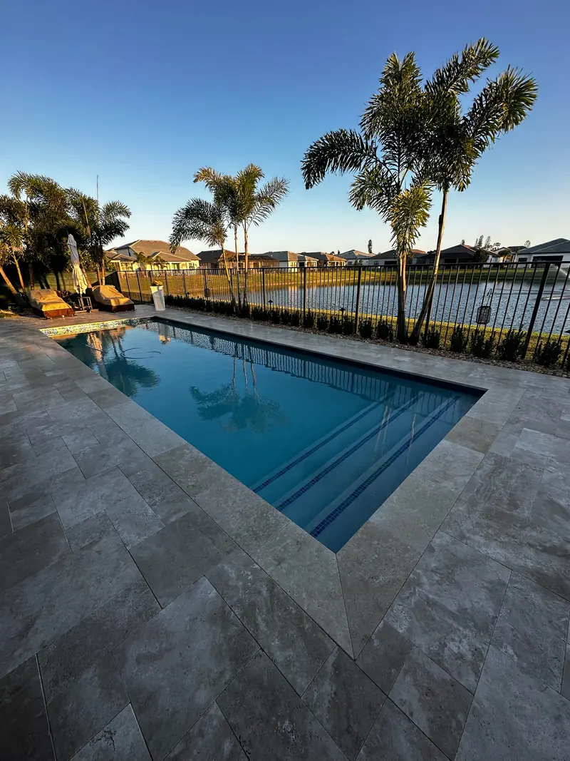Pool with a travertine-style deck facing a lake at sunset