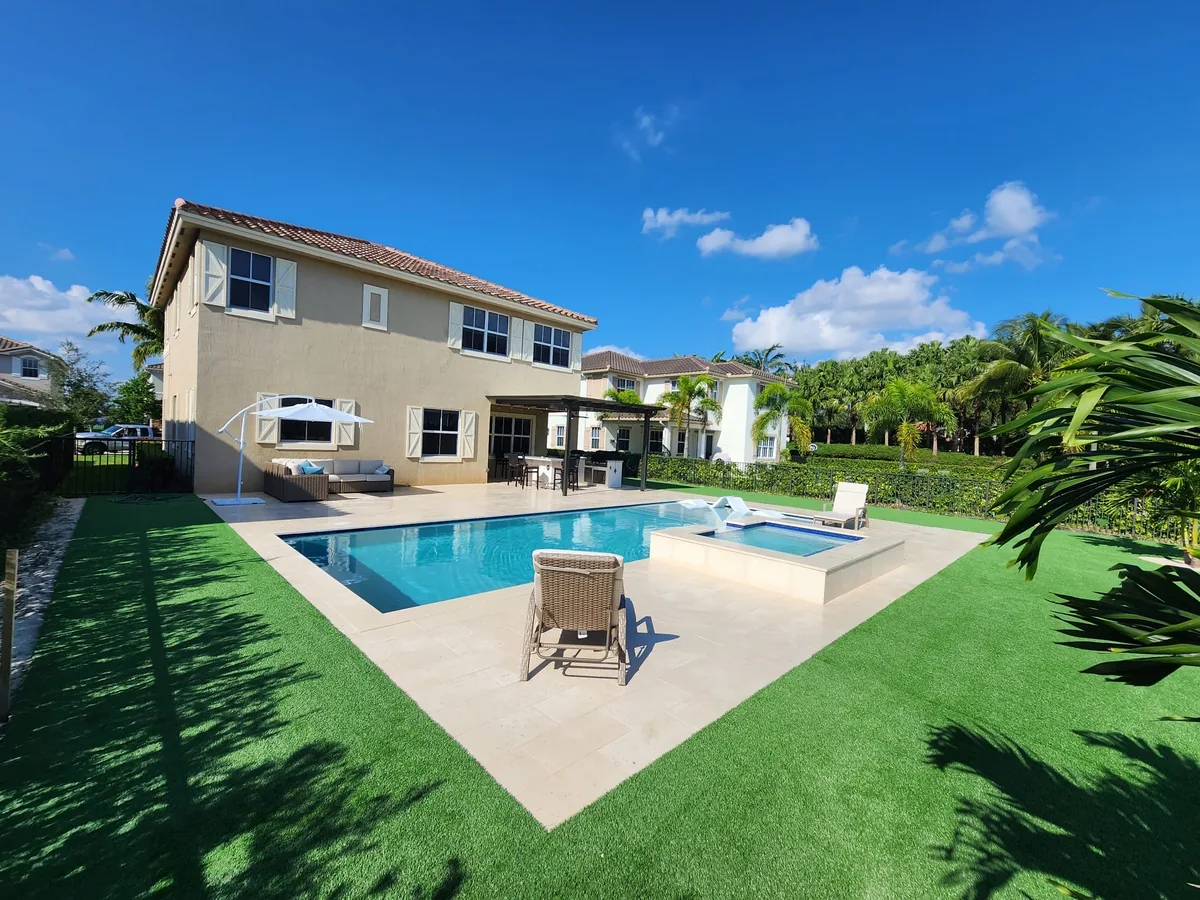 Two-story home with a pool, attached spa, beige pavers and turf