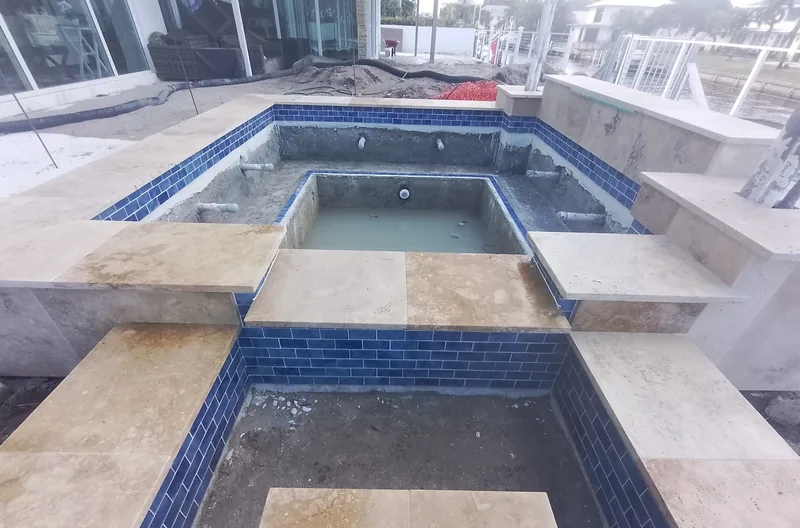 Travertine slabs bridging a tiled spa, seen from above, still under construction