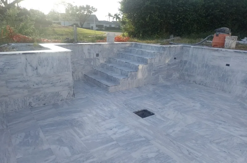 Stone-lined pool shell with new steps and an empty floor drain during construction