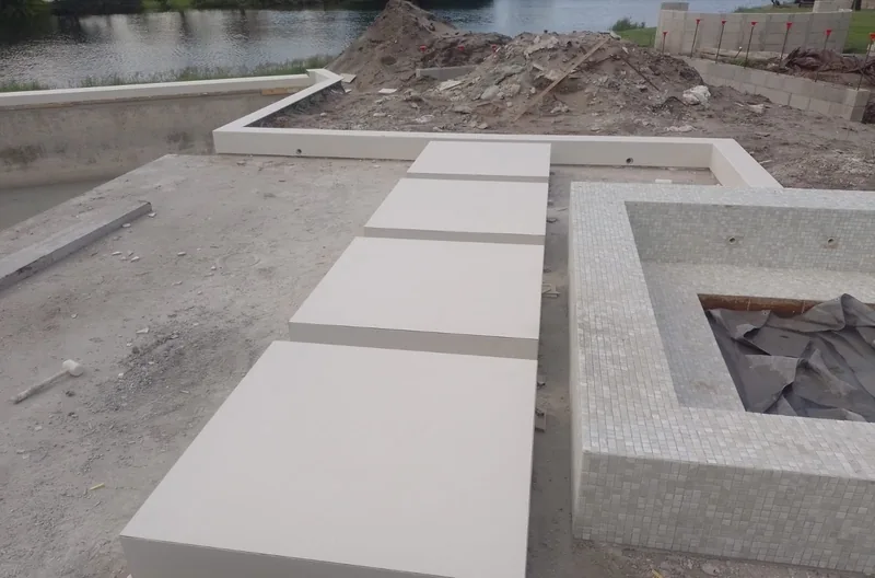 Large cream slabs set as steps and bench beside a pool being built at the edge of a lake
