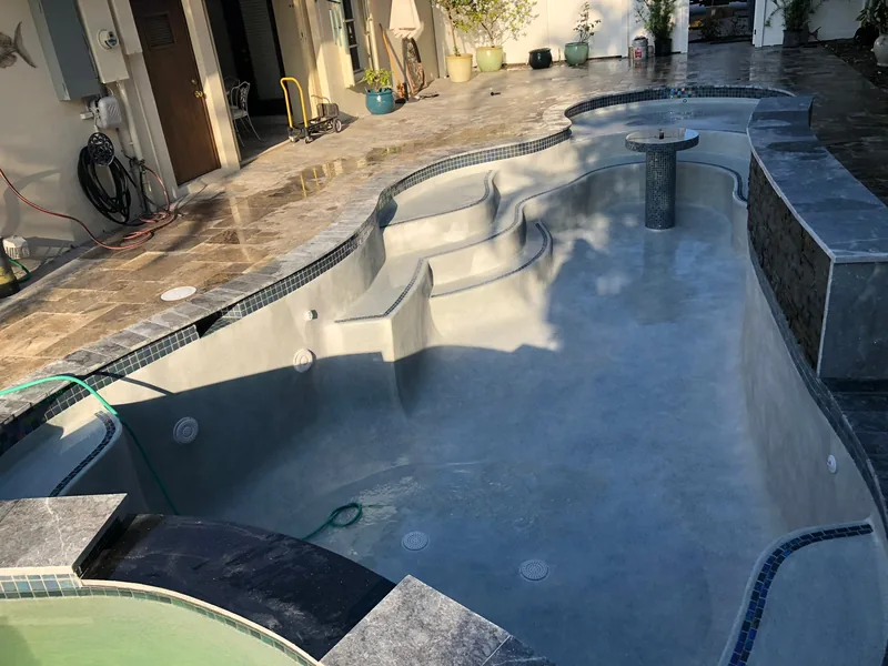 Freeform pool with a dark interior, stepped bench and stone coping
