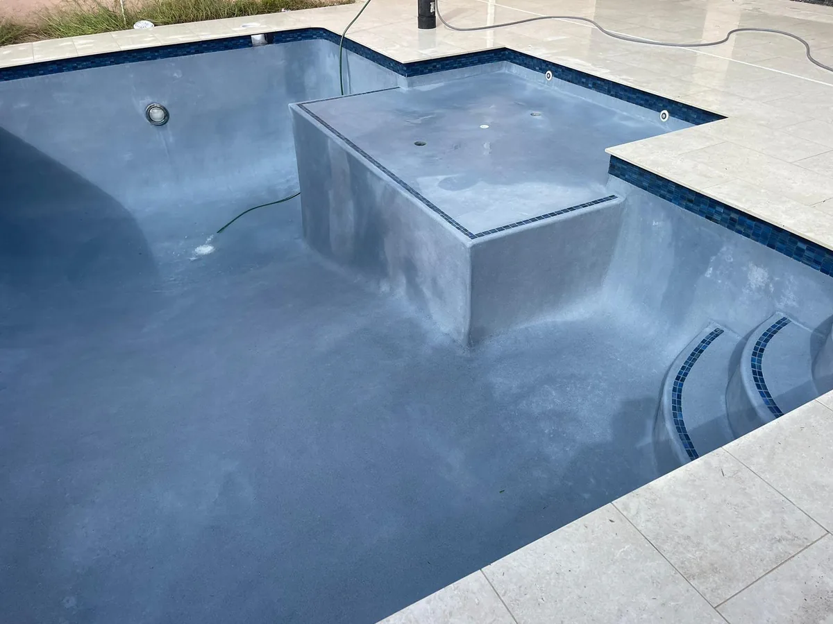 Pool with a raised block feature and tile border on a light stone deck