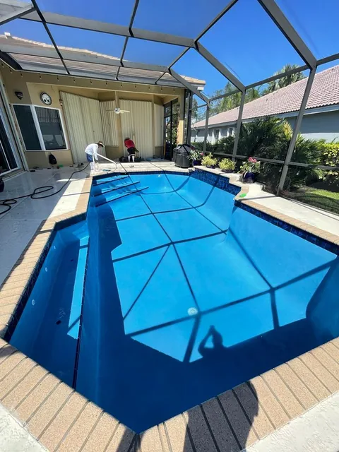 Blue pool inside a screened enclosure with a light deck