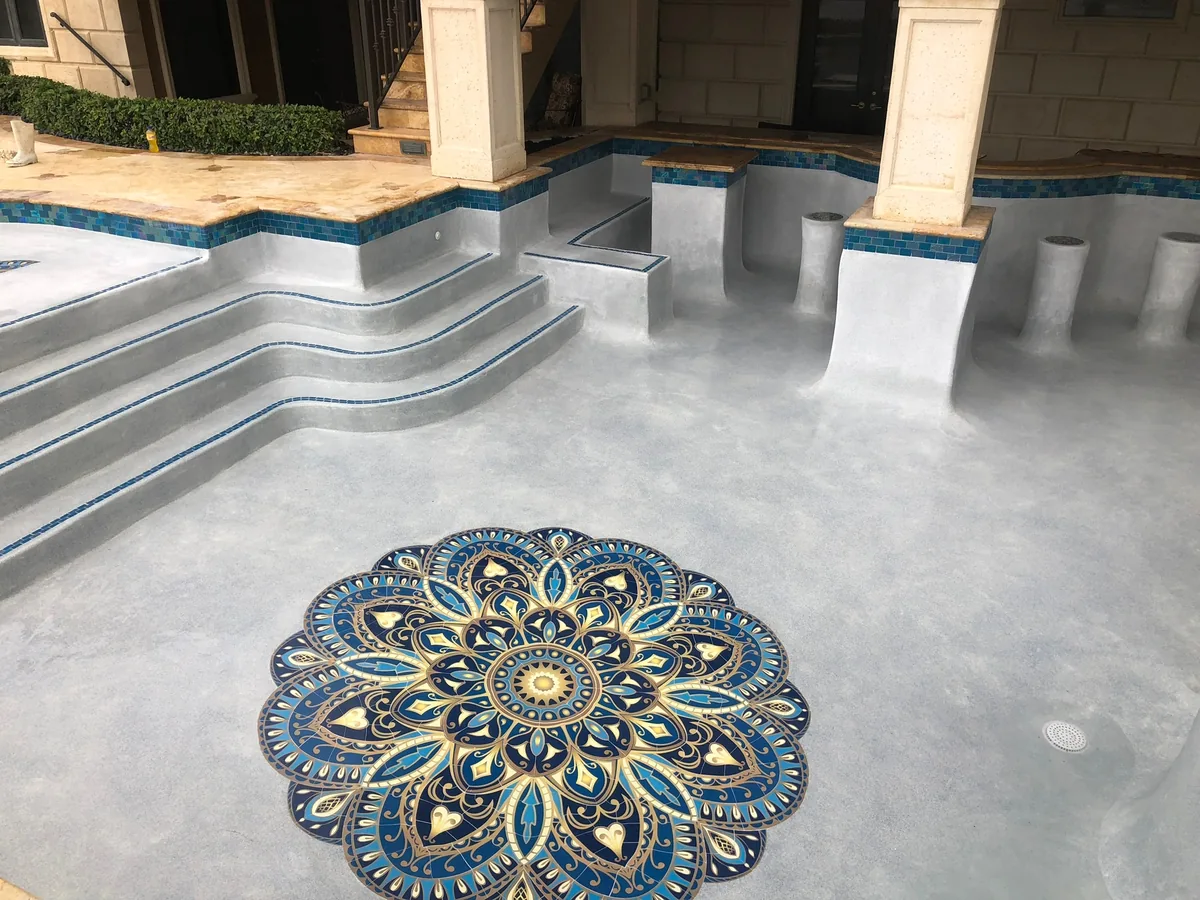 Round blue and gold mosaic medallion set into the floor at the foot of pool steps