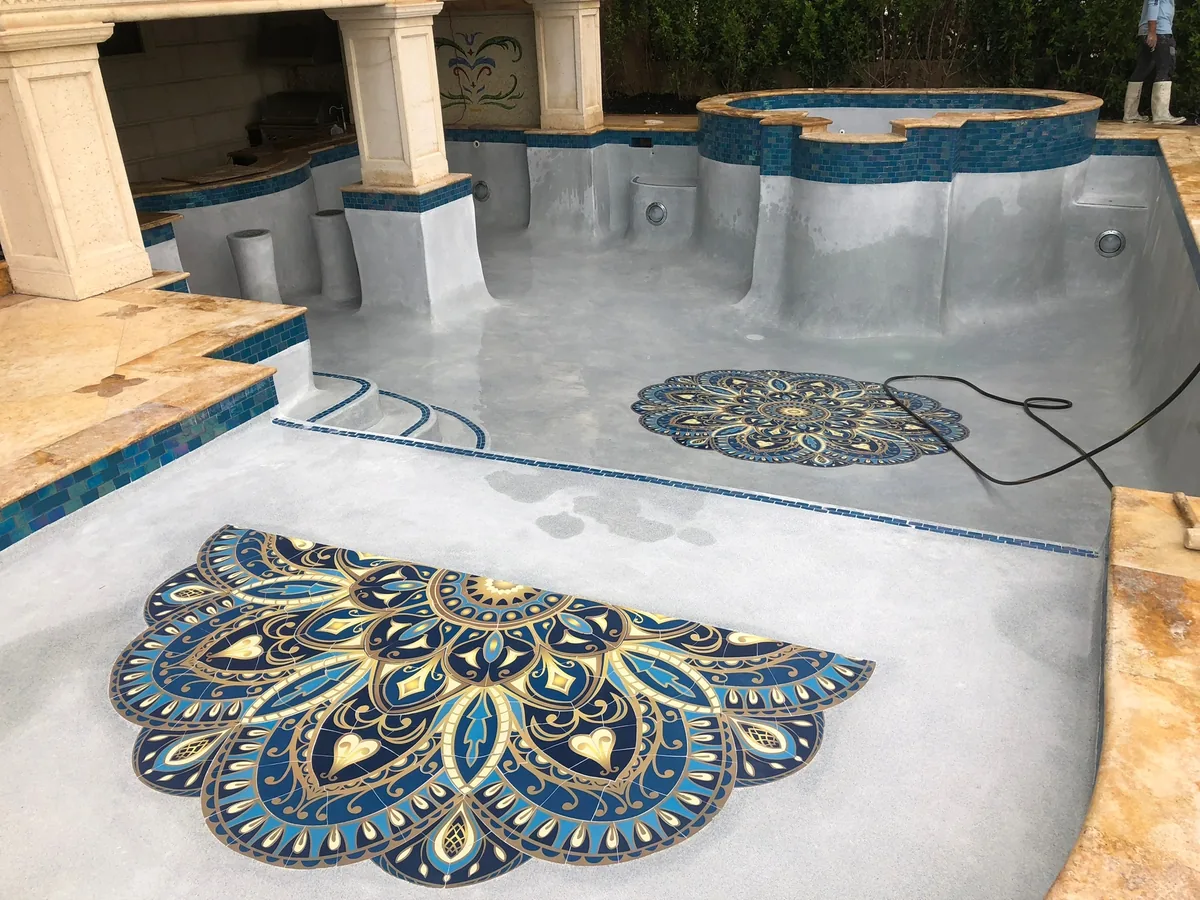 Two blue and gold mosaic medallions on the floor of a pool with a raised spa behind