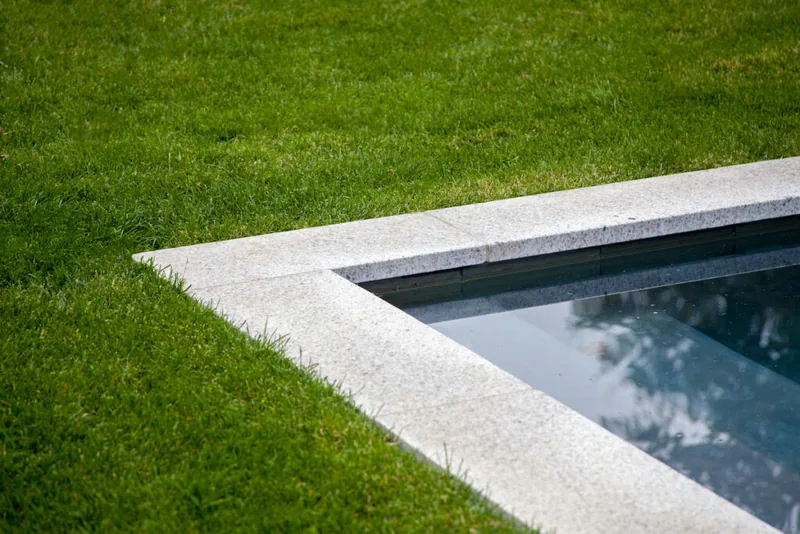 Close-up of light stone coping meeting the lawn at the pool edge