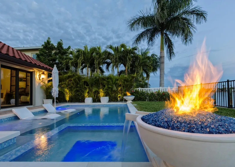 Fire bowl burning beside a lit spa and pool with in-pool loungers at dusk