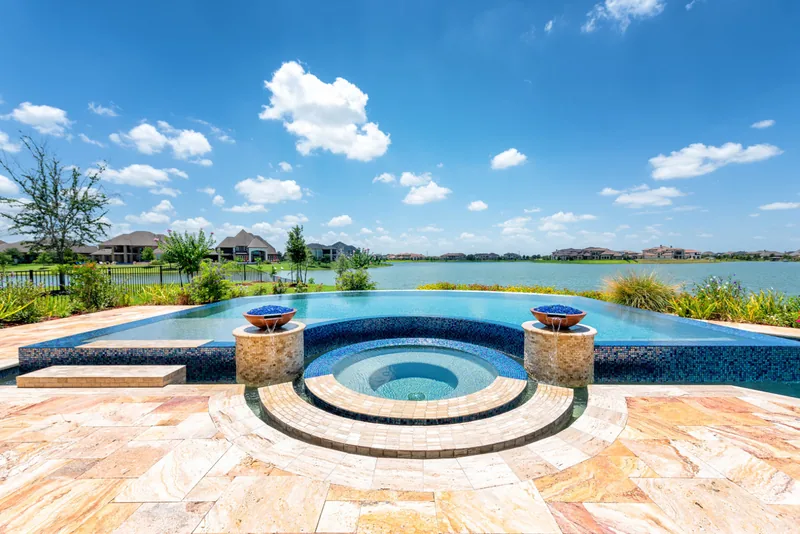 Circular spa between two fire bowls on a pool edge facing a lake