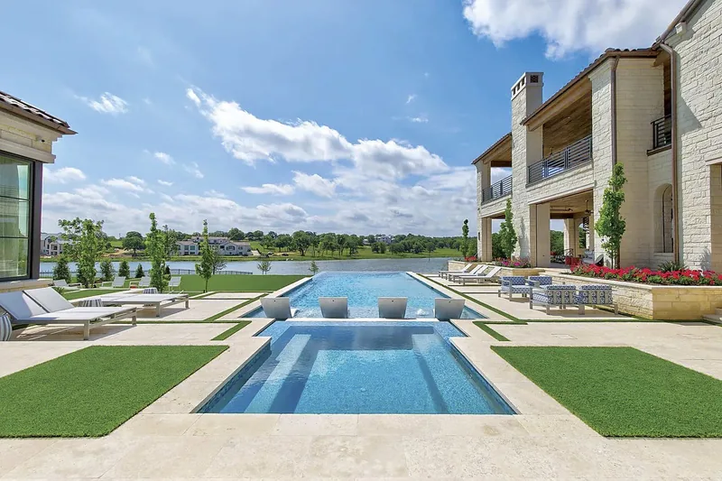 Long pool with turf strips, in-pool loungers and a stone two-story home