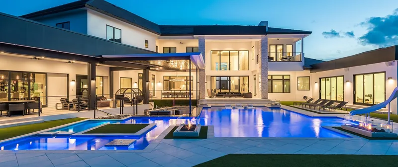 Large modern home at night with a long lit pool and spa