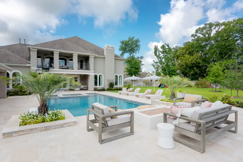 Pool with a white lounge set and planters in front of a two-story home