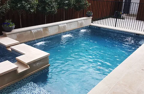 Raised spa wall with three sheer descents pouring into a blue pool