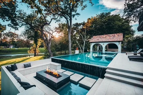 Sunken fire lounge beside a vanishing-edge pool under oak trees