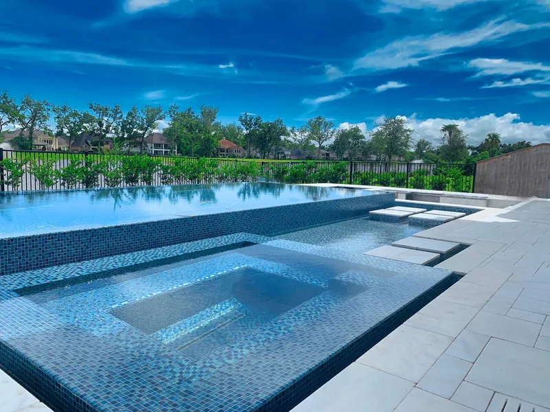 Tiled sun shelf and spa in a long pool, with a lake and tree line beyond