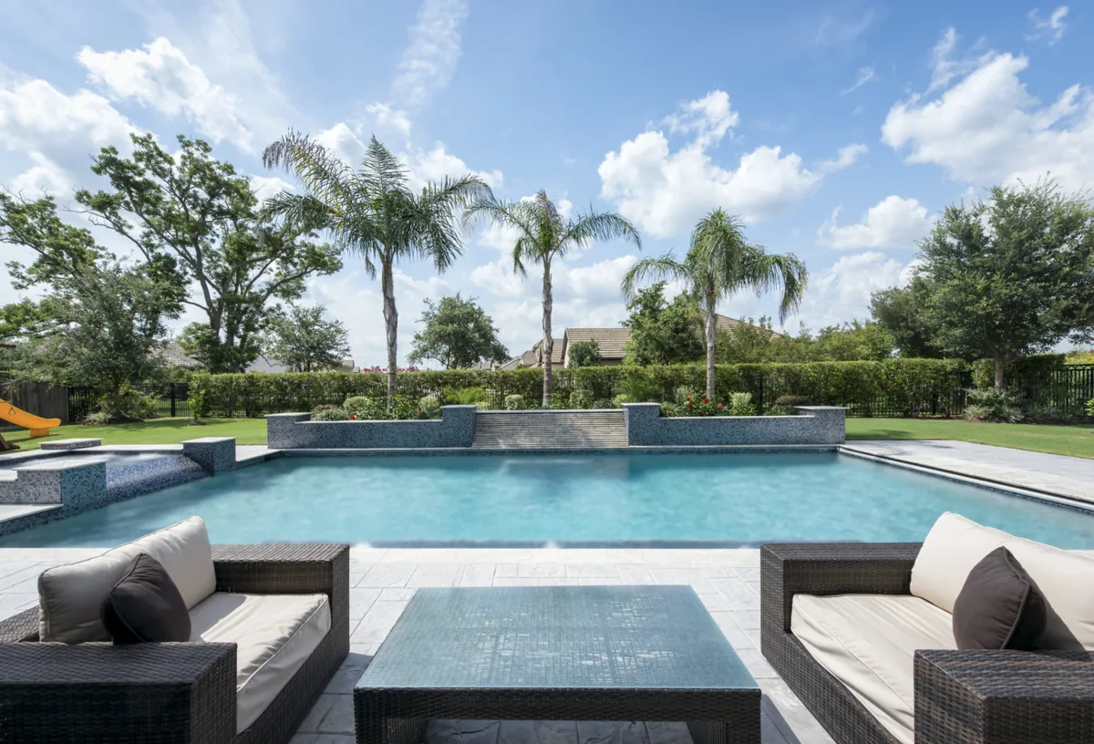 Wide pool lined with palms, seen from an outdoor lounge with sofas and a coffee table