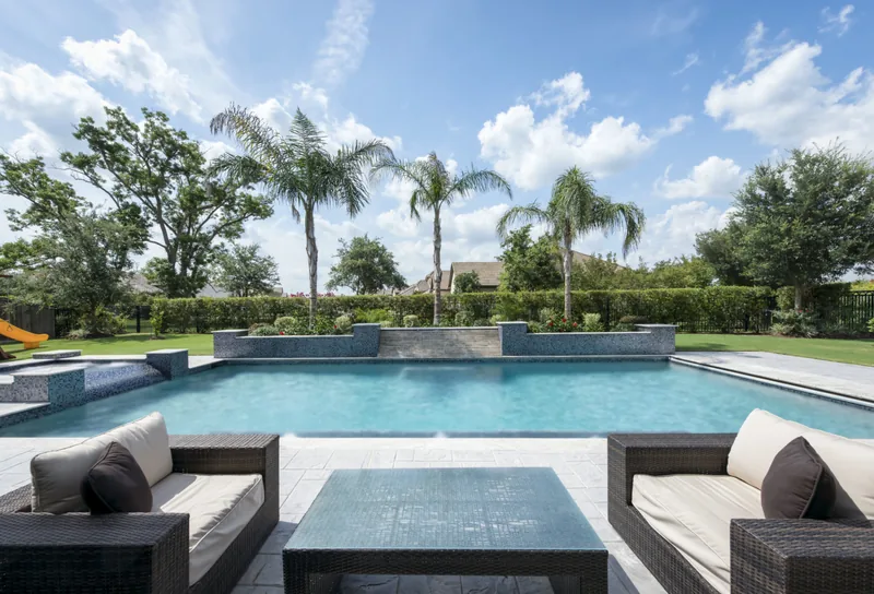 Wide pool lined with palms, seen from an outdoor lounge with sofas and a coffee table