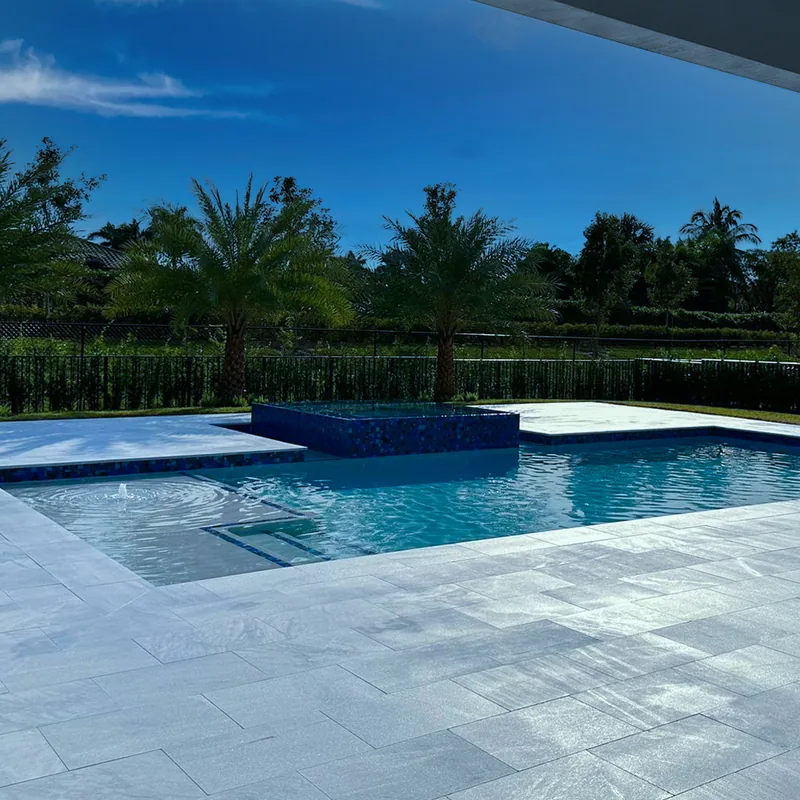 Rectangular pool with a raised spa and light stone coping and decking under a blue sky