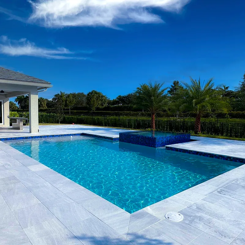 Clear blue pool with a tiled raised spa and wide light stone coping next to a covered patio
