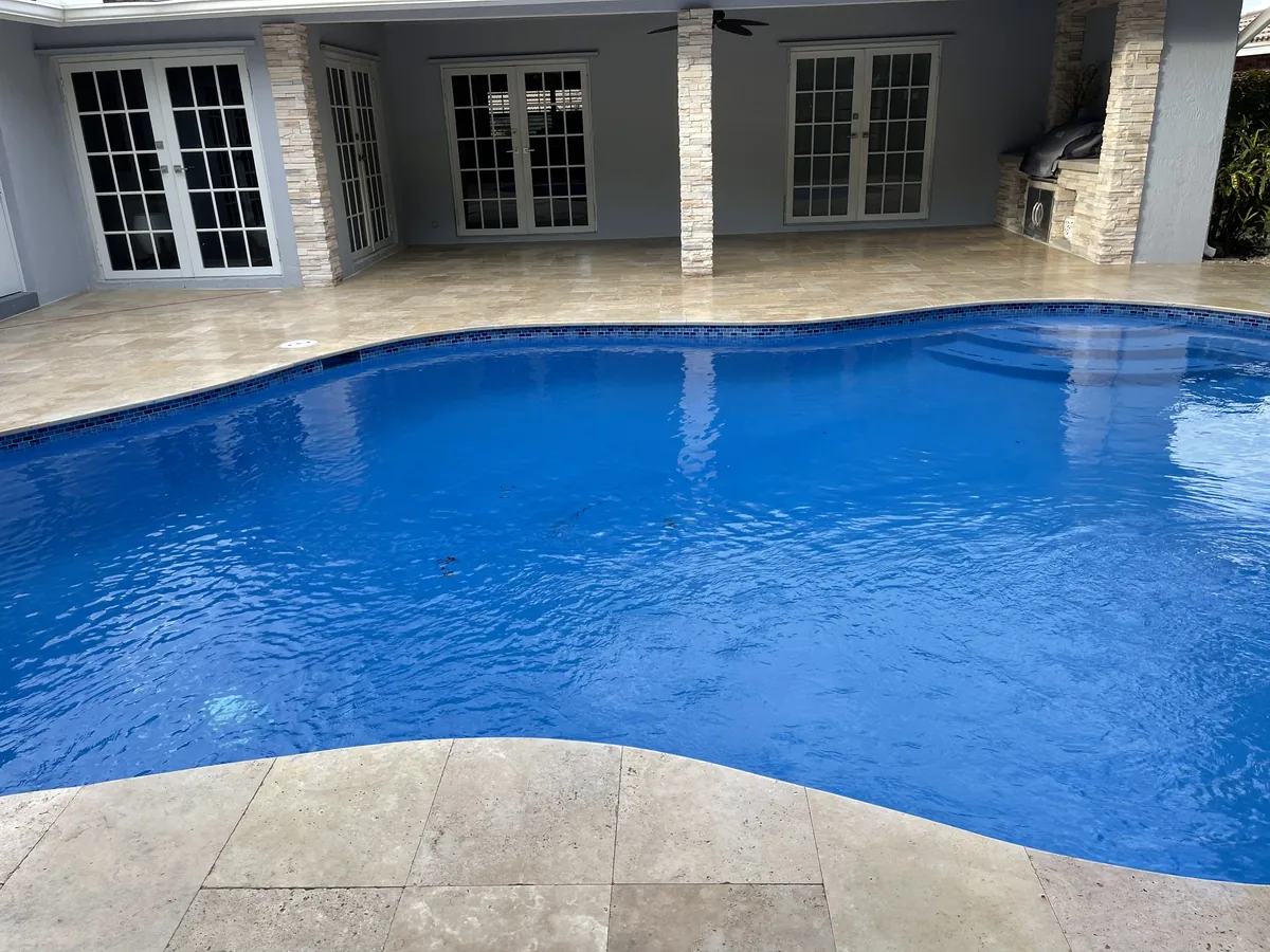 After: deep-blue water and travertine coping in front of the covered lanai