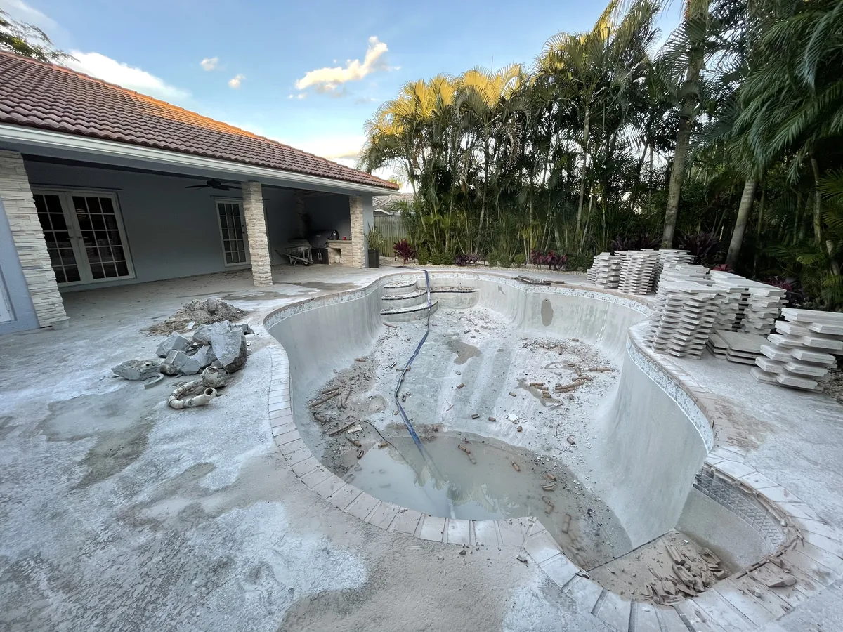 Before: the old freeform pool drained, coping removed and stacked, in a yard of palms