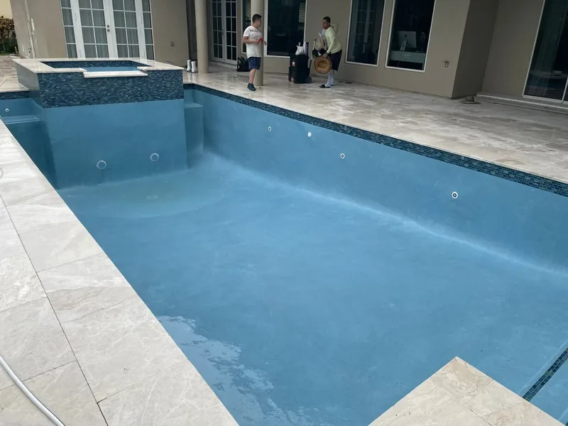 Rectangular pool and attached spa with travertine coping during the fill