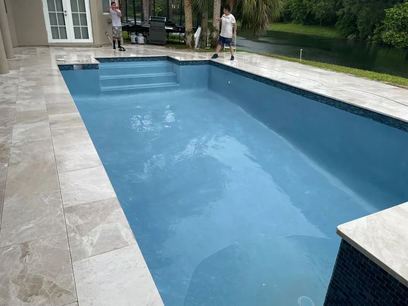 Rectangular pool with a fresh finish, travertine deck and coping, being filled