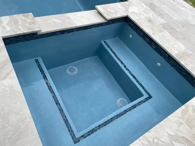 Spa with a blue tile line and travertine coping after resurfacing
