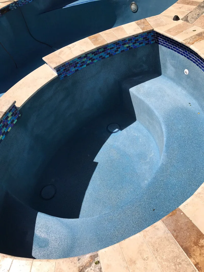 Dark-finished spa with curved seating and a blue tile waterline in stone coping