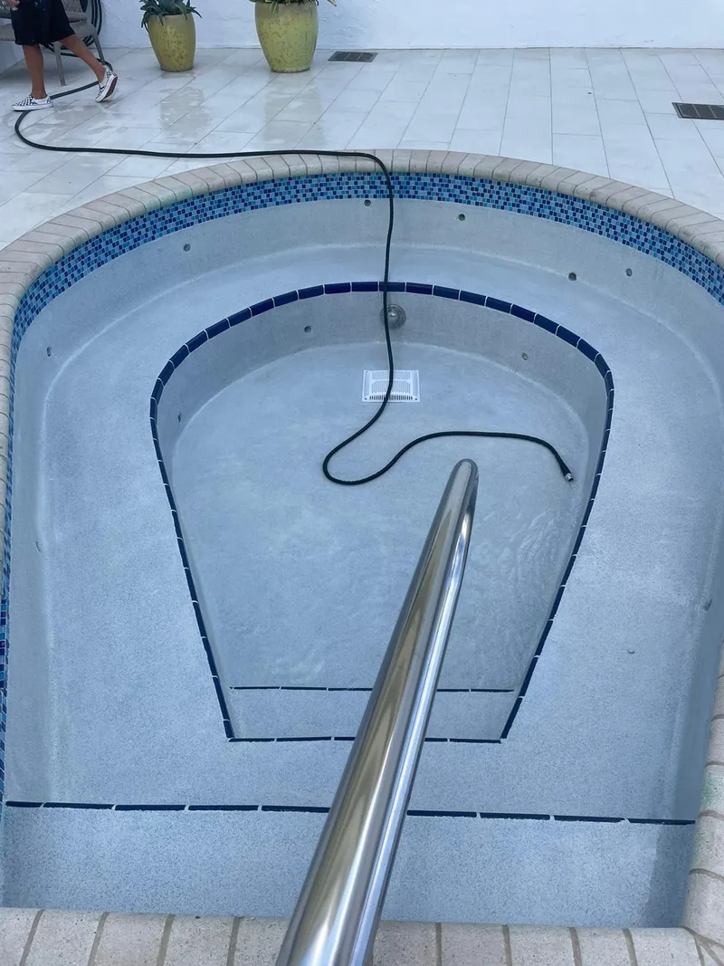 Round spa with a stainless steel handrail and a blue tile band under white coping