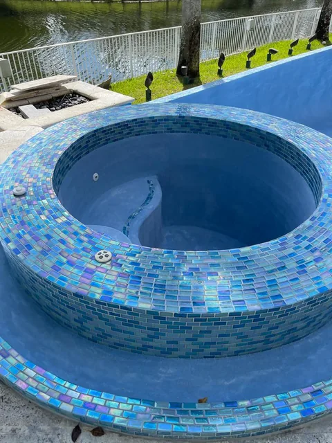 Round raised spa with blue iridescent glass tile beside a lake