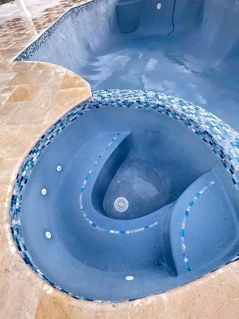 Curved spa with a bench seat and a band of blue mosaic tile below the coping
