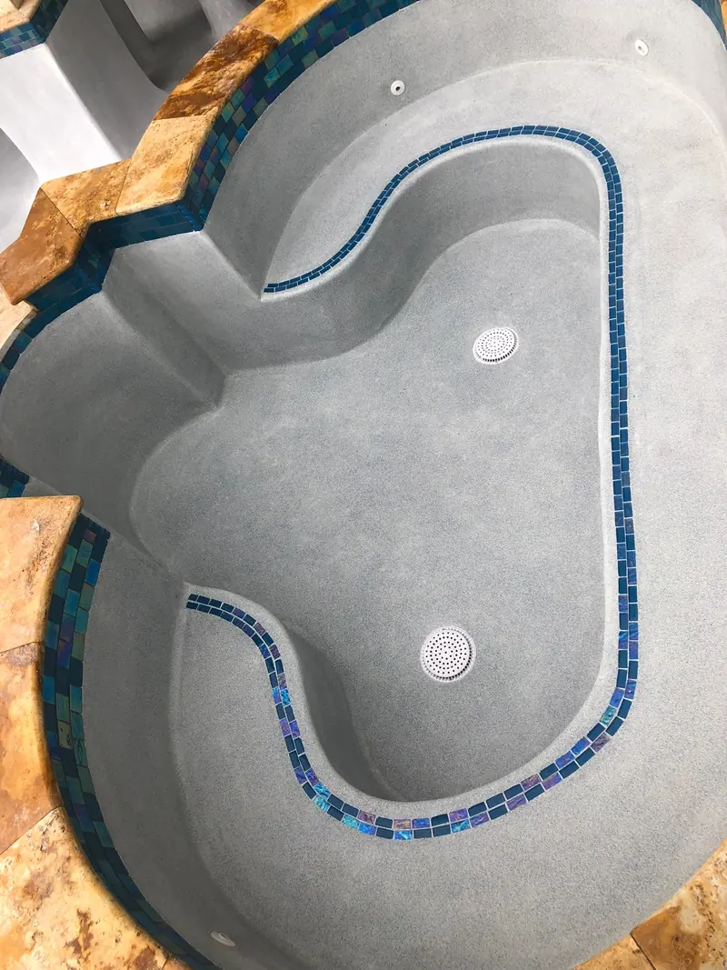 Free-form spa with a blue mosaic tile line and warm stone coping