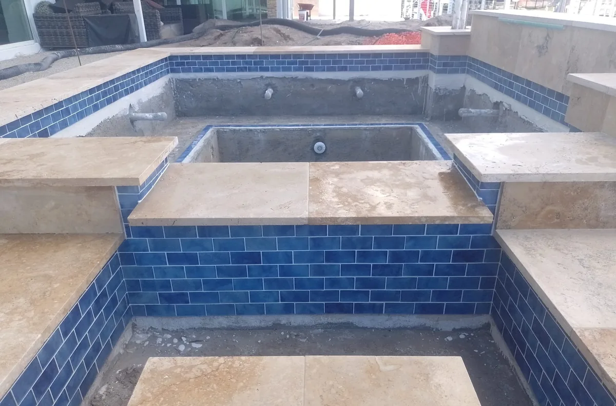 Raised spa lined with blue tile and capped with travertine coping pieces