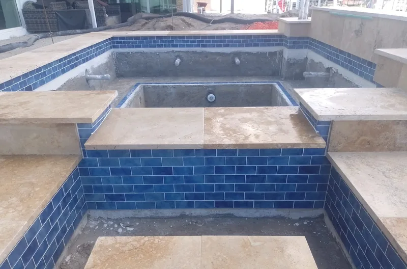 Raised spa lined with blue tile and capped with travertine coping pieces